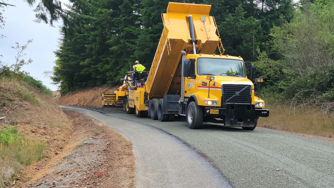 A dump truck feeding a paver resurfacing a rural road