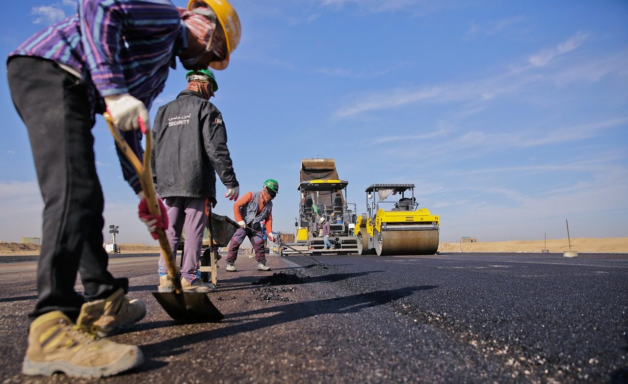 A paving crew laying and raking fresh asphalt behind a roller